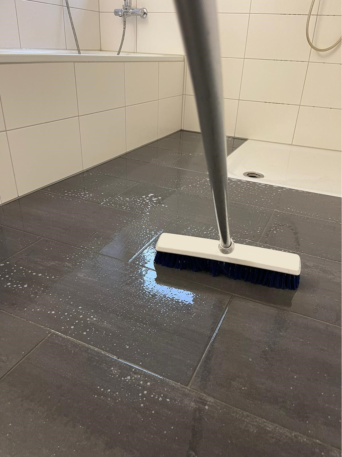 Bodenbürste auf nassen dunklen Duschfliesen